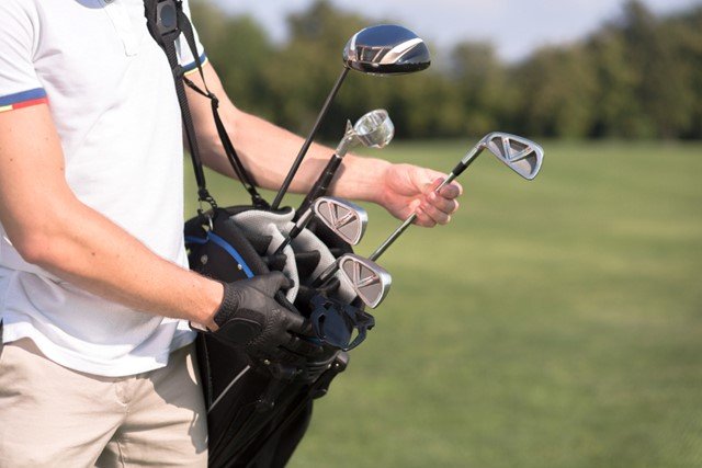 a golfer is carrying his black golf bag with full golf clubs 