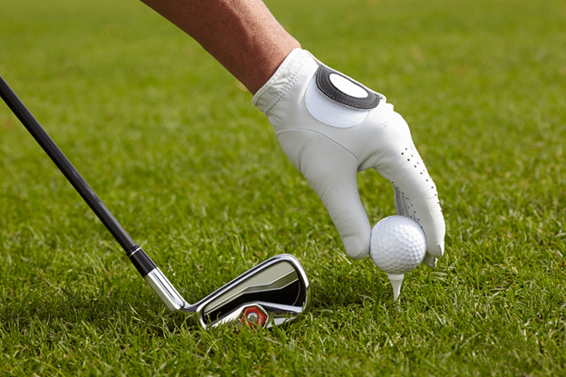 a golf player adjusts his ball before hitting and golf bat on his hand