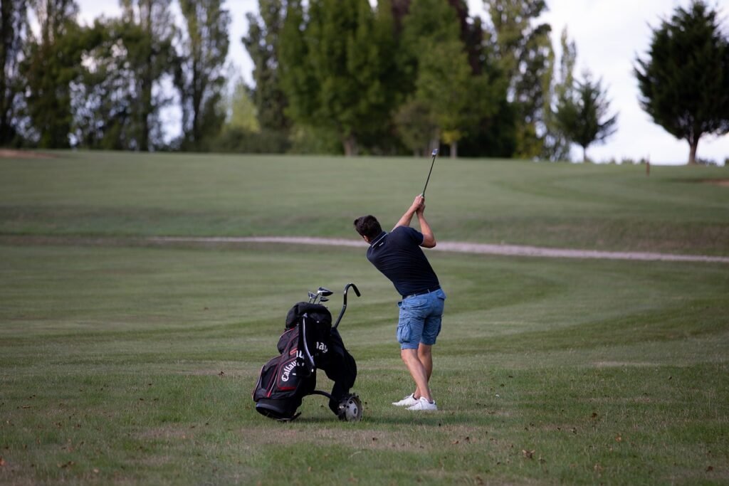 one boy is playing golf in wintertime in a open field where he has his golf bag, golf bat and golf ball.