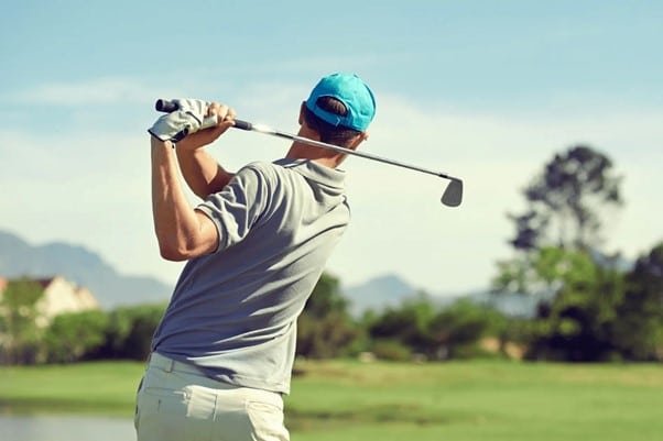a golfer is trying to hit golf ball in a golf course wearing white golf caps representing Golf Caps for Men. 