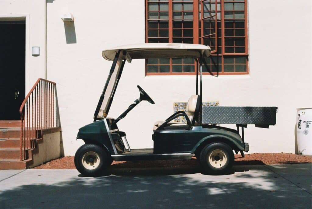A stationary green golf cart parked by a building on a sunny day.