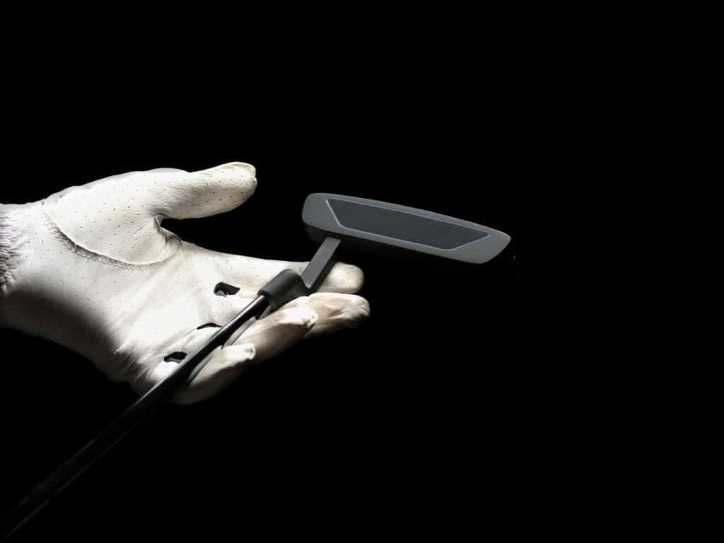 A close-up image focusing on a golf putter held by a gloved hand against a black background.