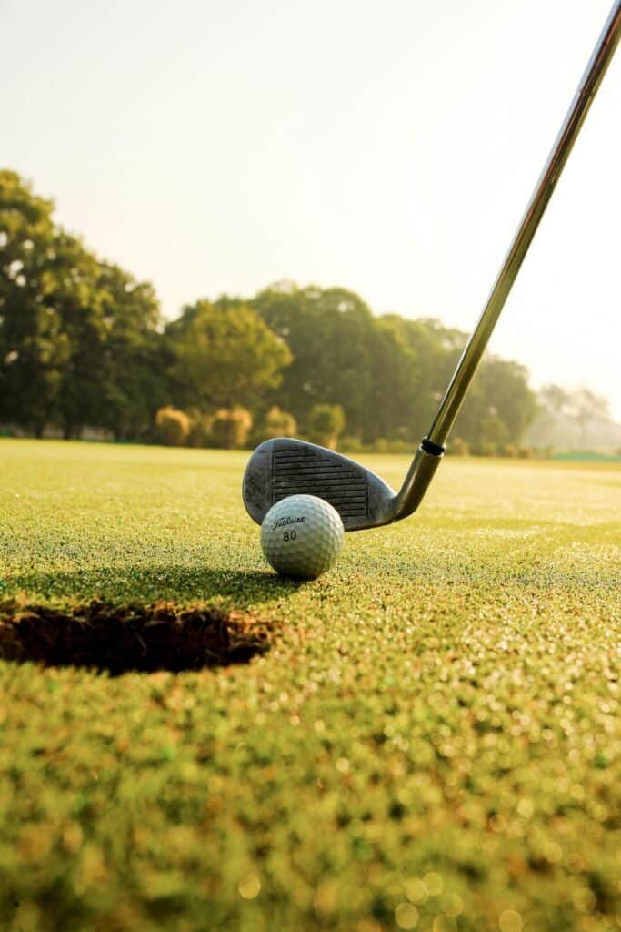 Closeup of golf ball placed on green grassy court against golf club under clear blue sky on sunny day